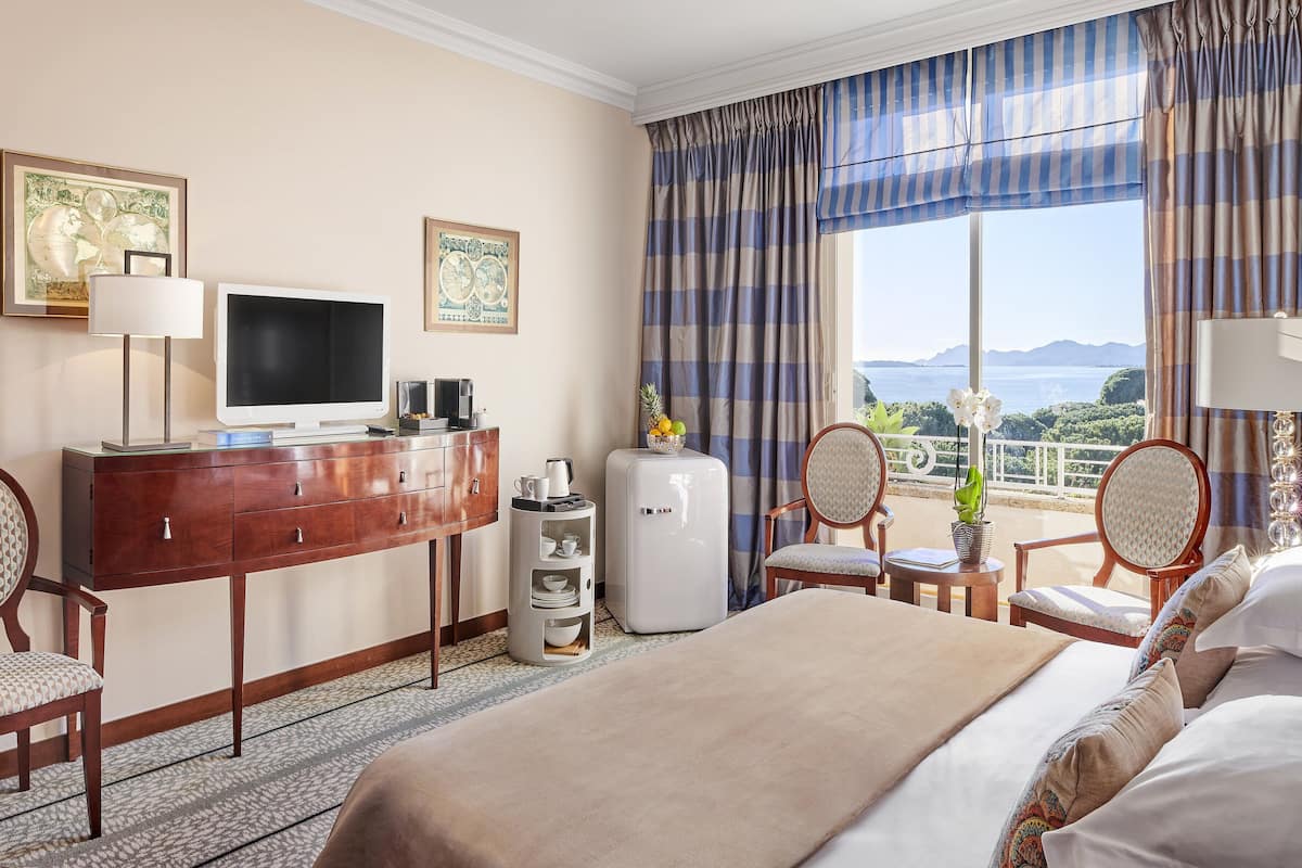Habitación de hotel con cama, escritorio con televisor, cafetera y vista al mar.
