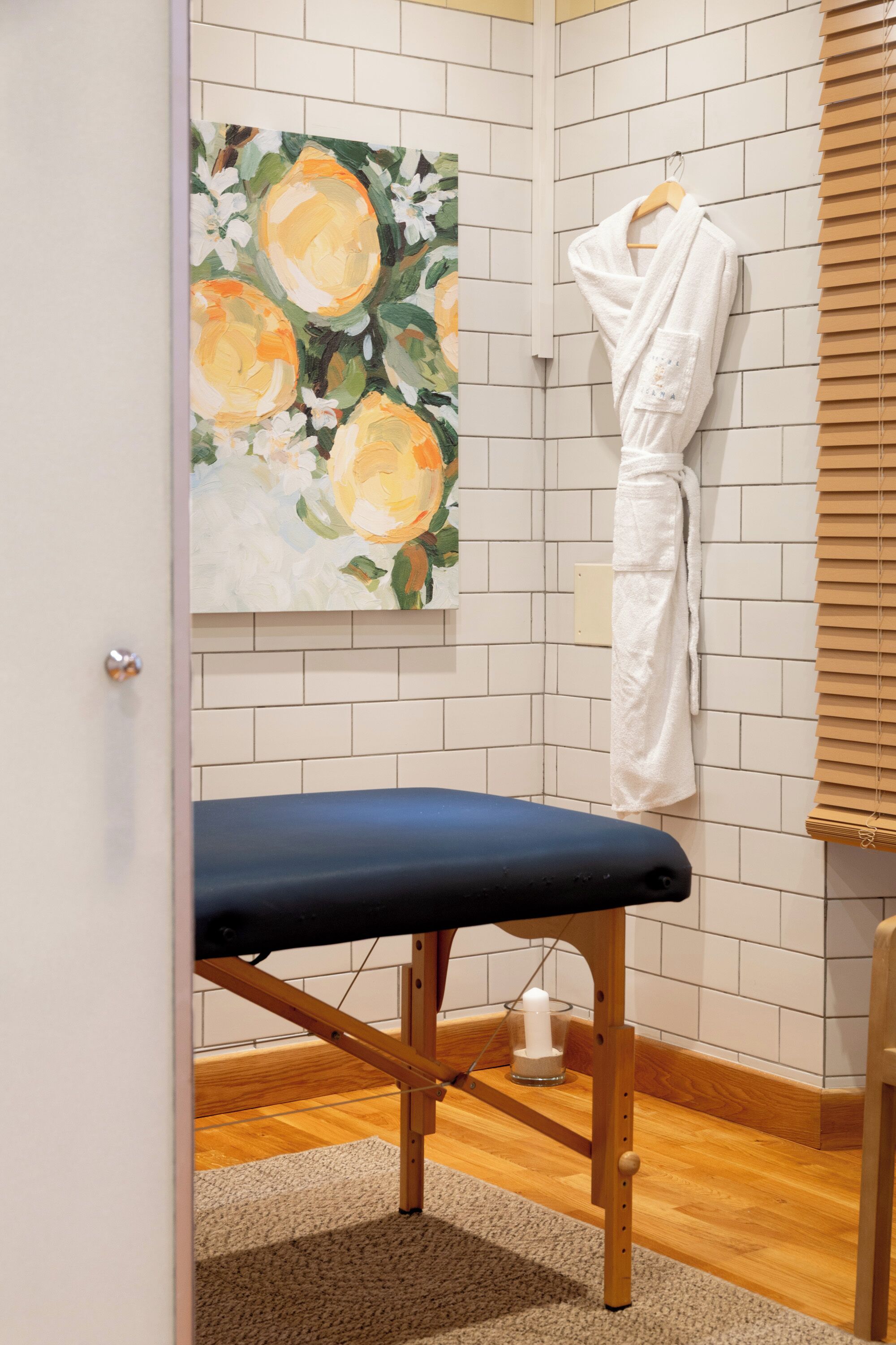 A room with a wooden bench, a white robe hanging on a rack, and a painting of flowers on the wall.