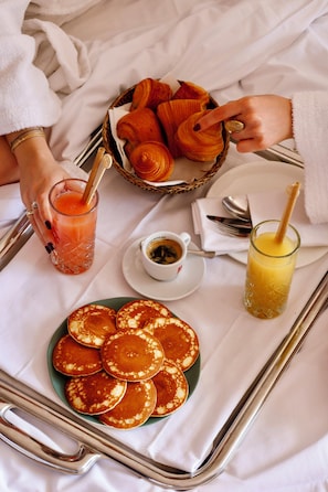 En bakke med pandekager, croissanter, et glas appelsinjuice og en kop kaffe.
