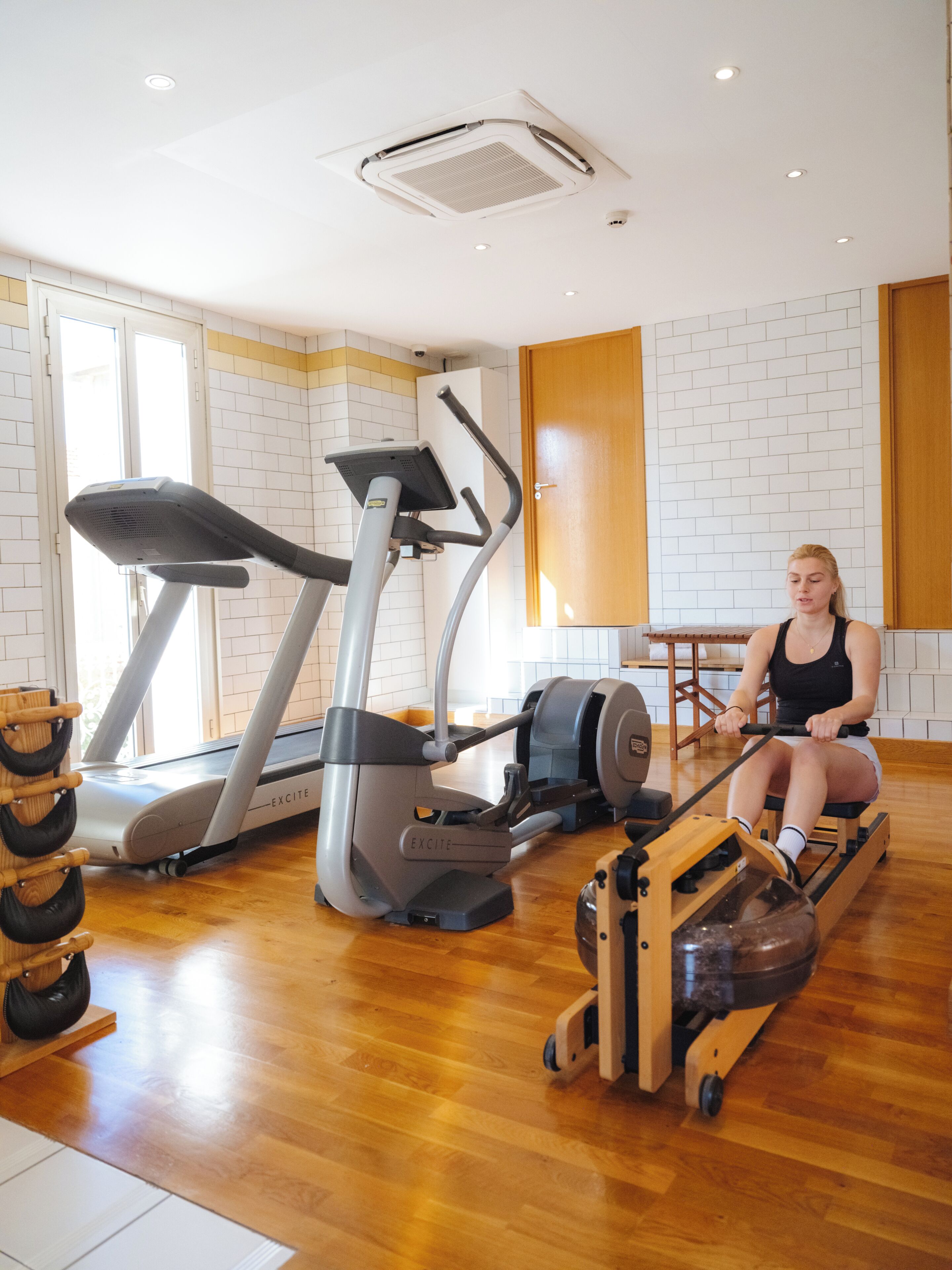 Une salle de sport équipée de matériel d’exercice, notamment un tapis de course et un rameur, et dotée d’un plancher en bois.
