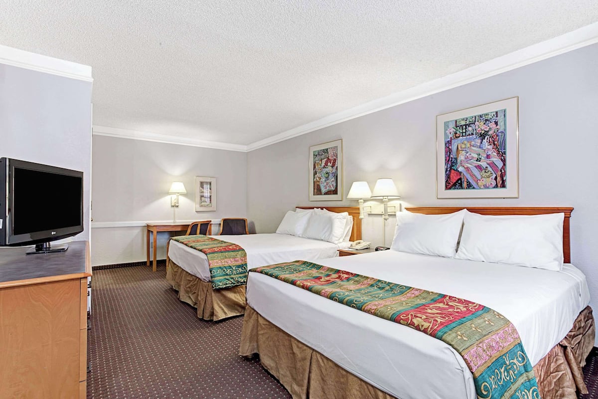 Ein Hotelzimmer mit zwei Betten, einem Schreibtisch, einem Fernseher und zwei Lampen.