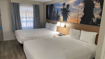 Habitación de hotel con dos camas, un ventanal con cortinas y una vista al atardecer en la pared.