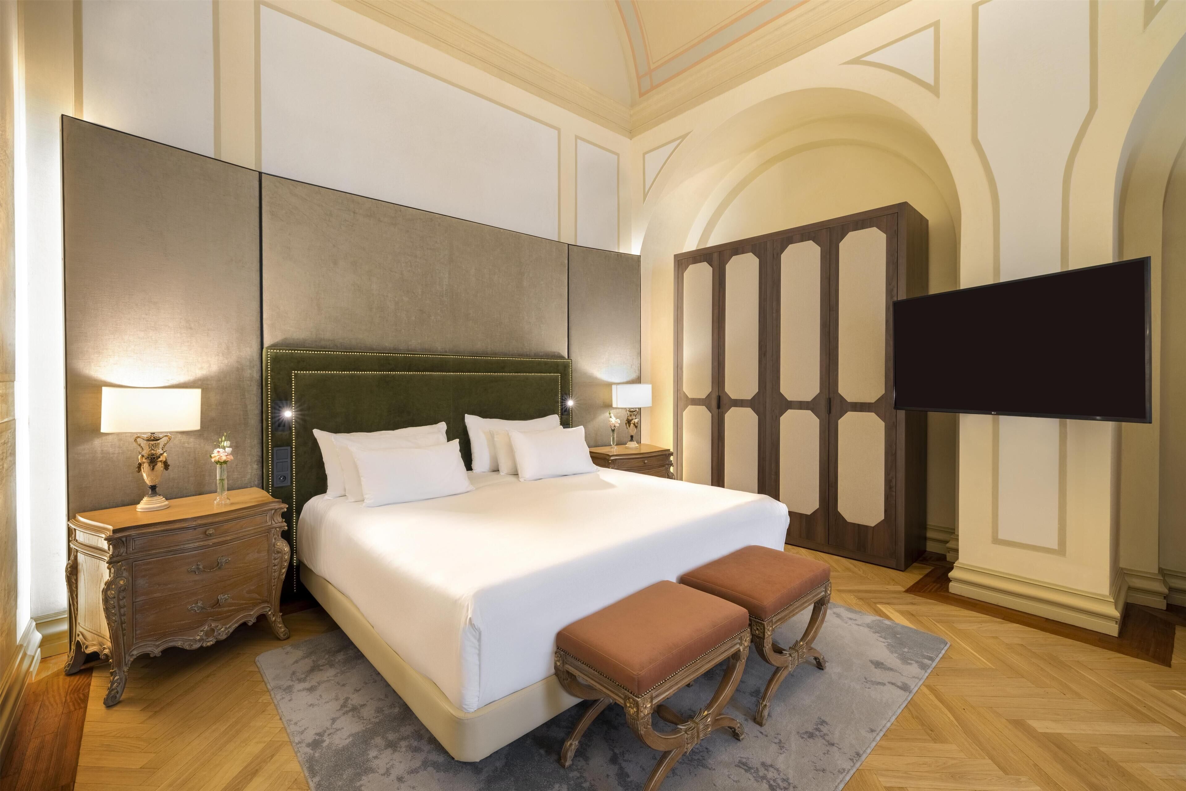 Habitación de hotel con una cama grande, dos mesitas de noche, un televisor de pantalla plana y un panel decorativo en la pared.