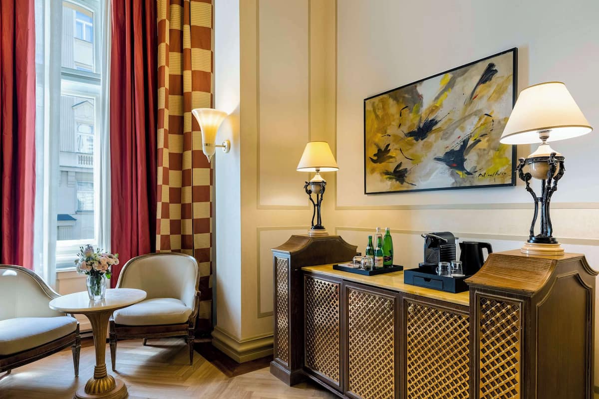 Un hall d’hôtel avec un comptoir d’accueil, deux chaises, une machine à café et un tableau accroché au mur.