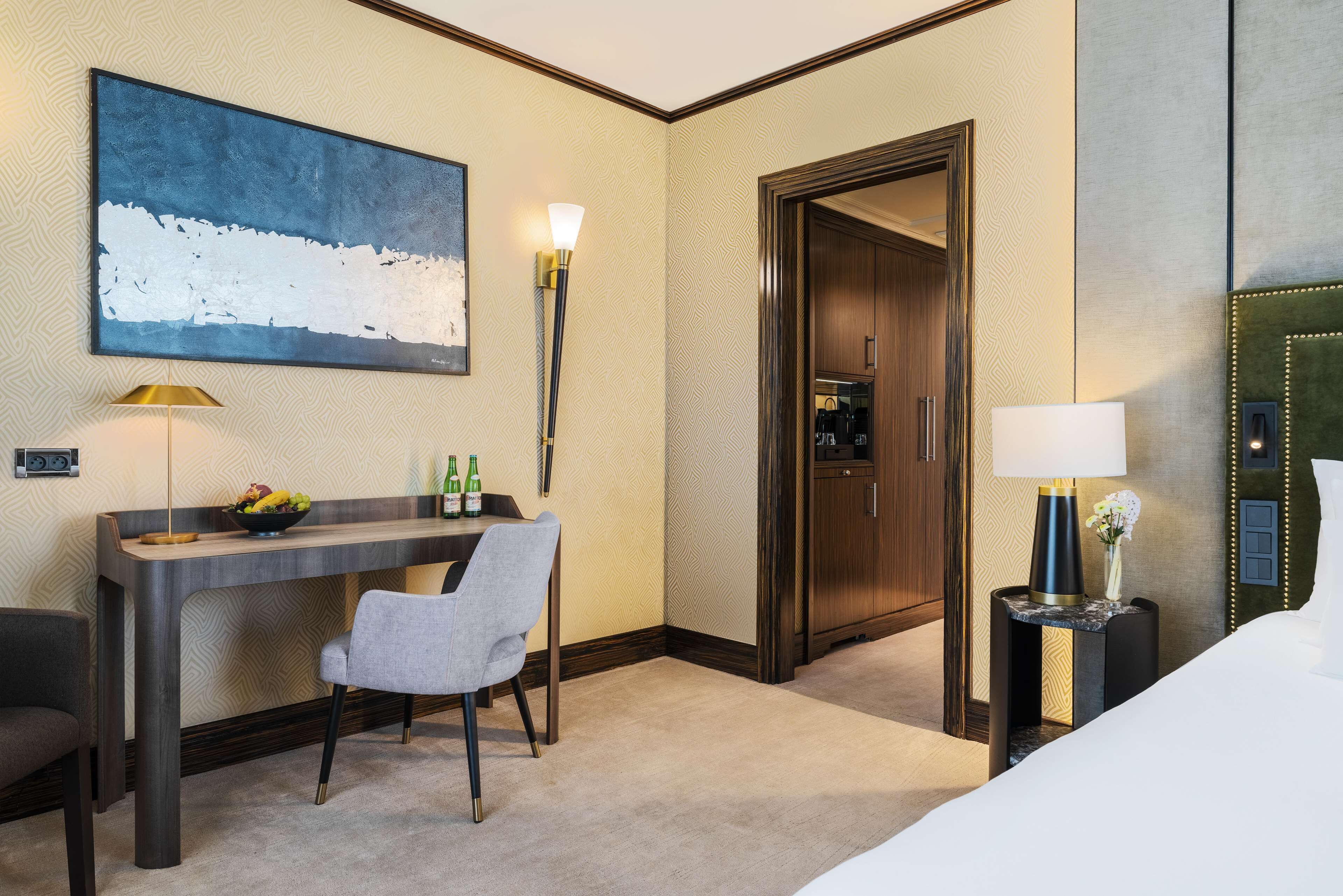 A hotel room with a desk, chair, bed, and a large abstract painting on the wall.