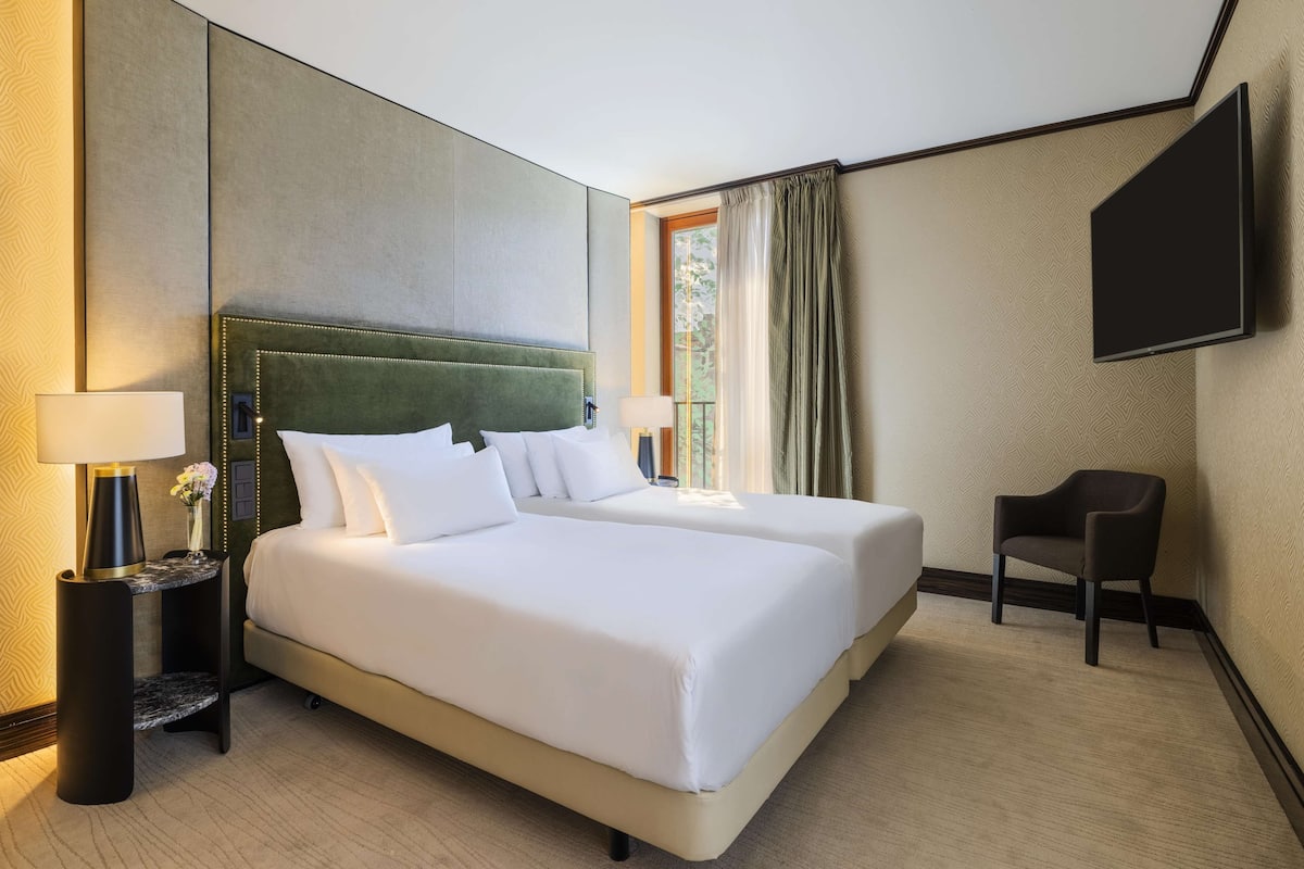 Une chambre d’hôtel avec un grand lit, deux tables de chevet avec des lampes, une chaise et un téléviseur à écran plat fixé au mur.