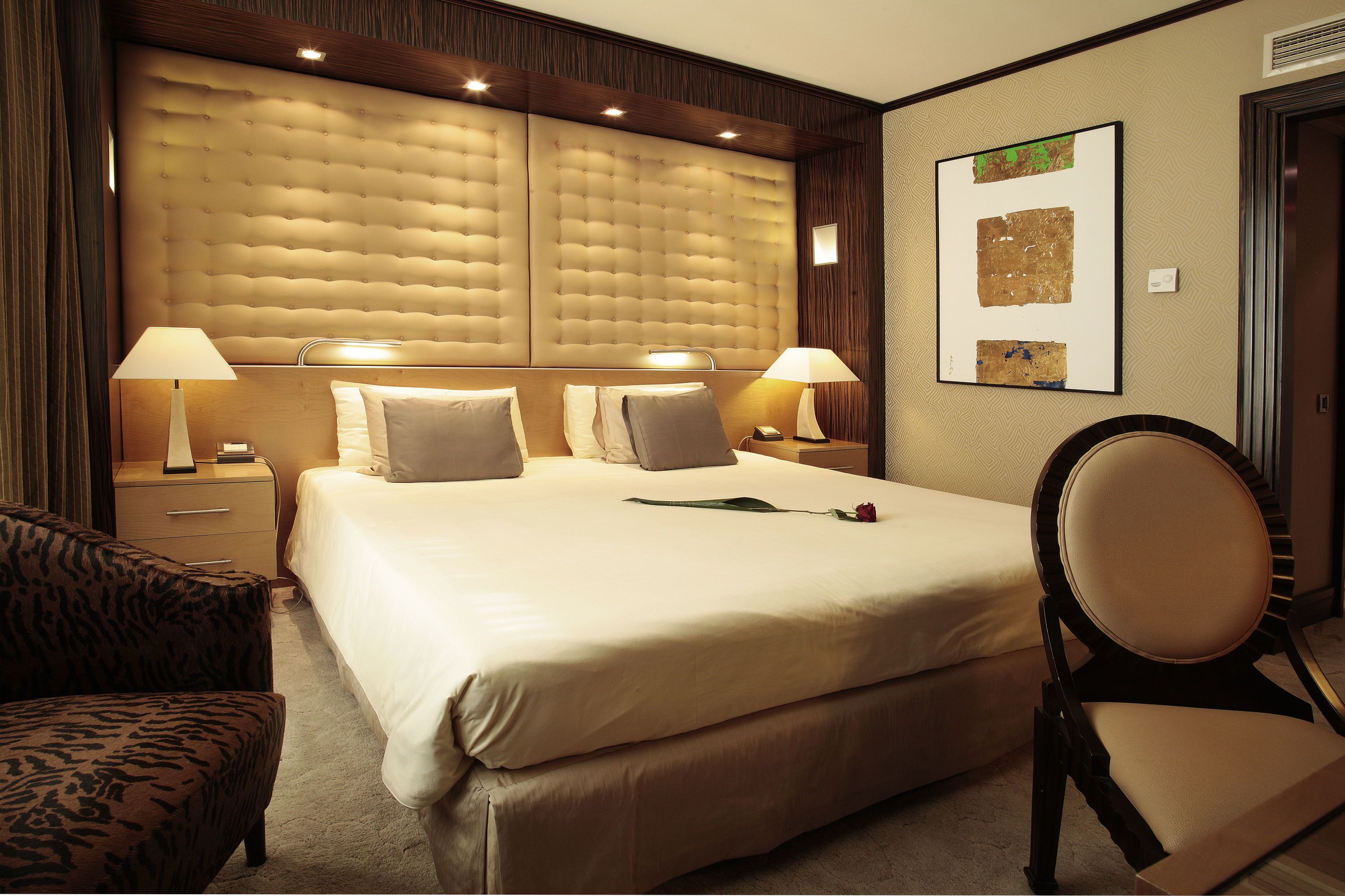 Quarto de hotel com uma cama grande, duas mesas de cabeceira com luminárias, uma cadeira e um quadro na parede.