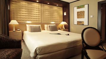 Quarto de hotel com uma cama grande, duas mesas de cabeceira com luminárias, uma cadeira e um quadro na parede.