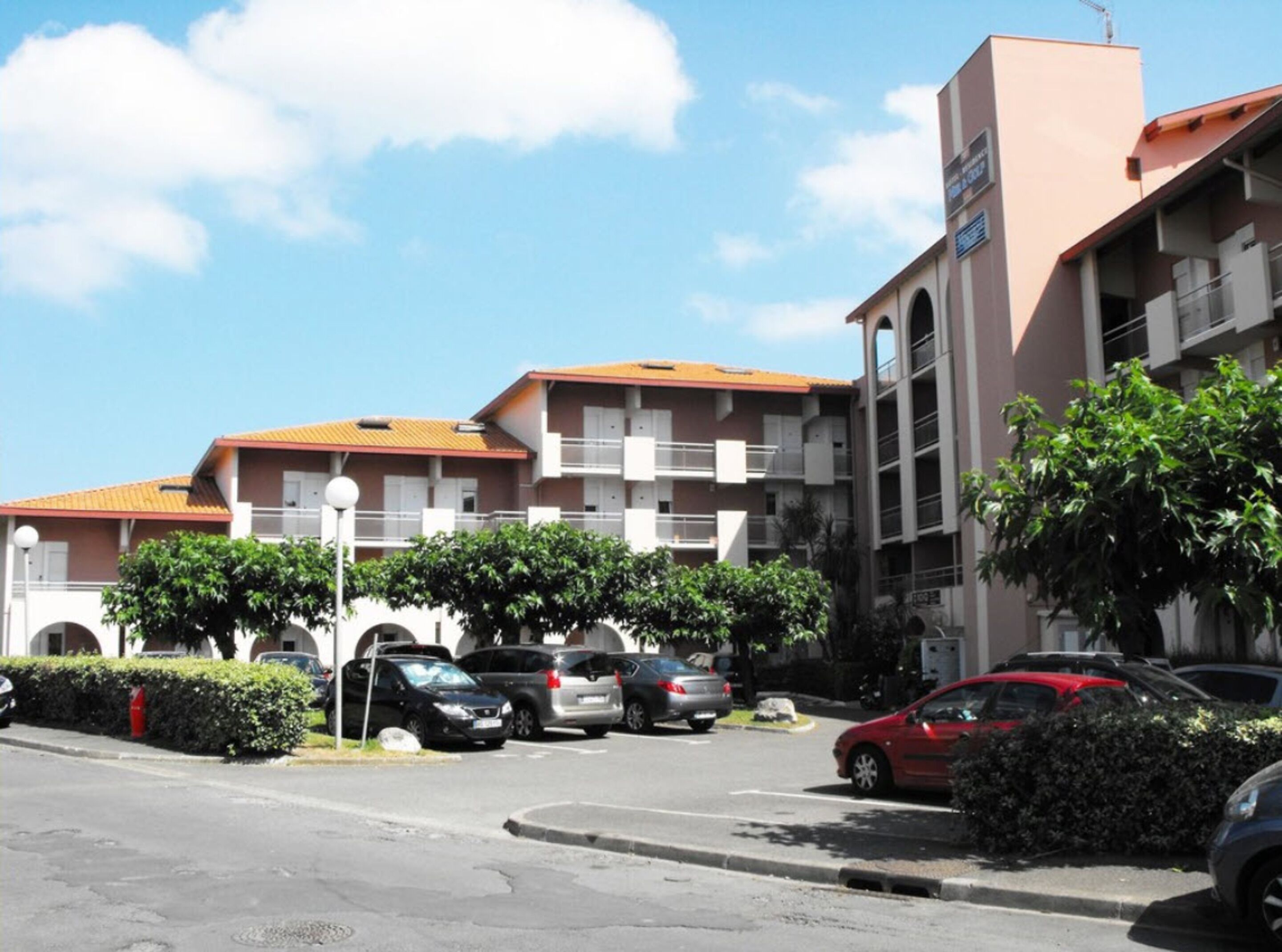 A multi-story building with balconies, a parking lot, and a clear sky.