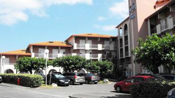 A multi-story building with balconies, a parking lot, and a clear sky.