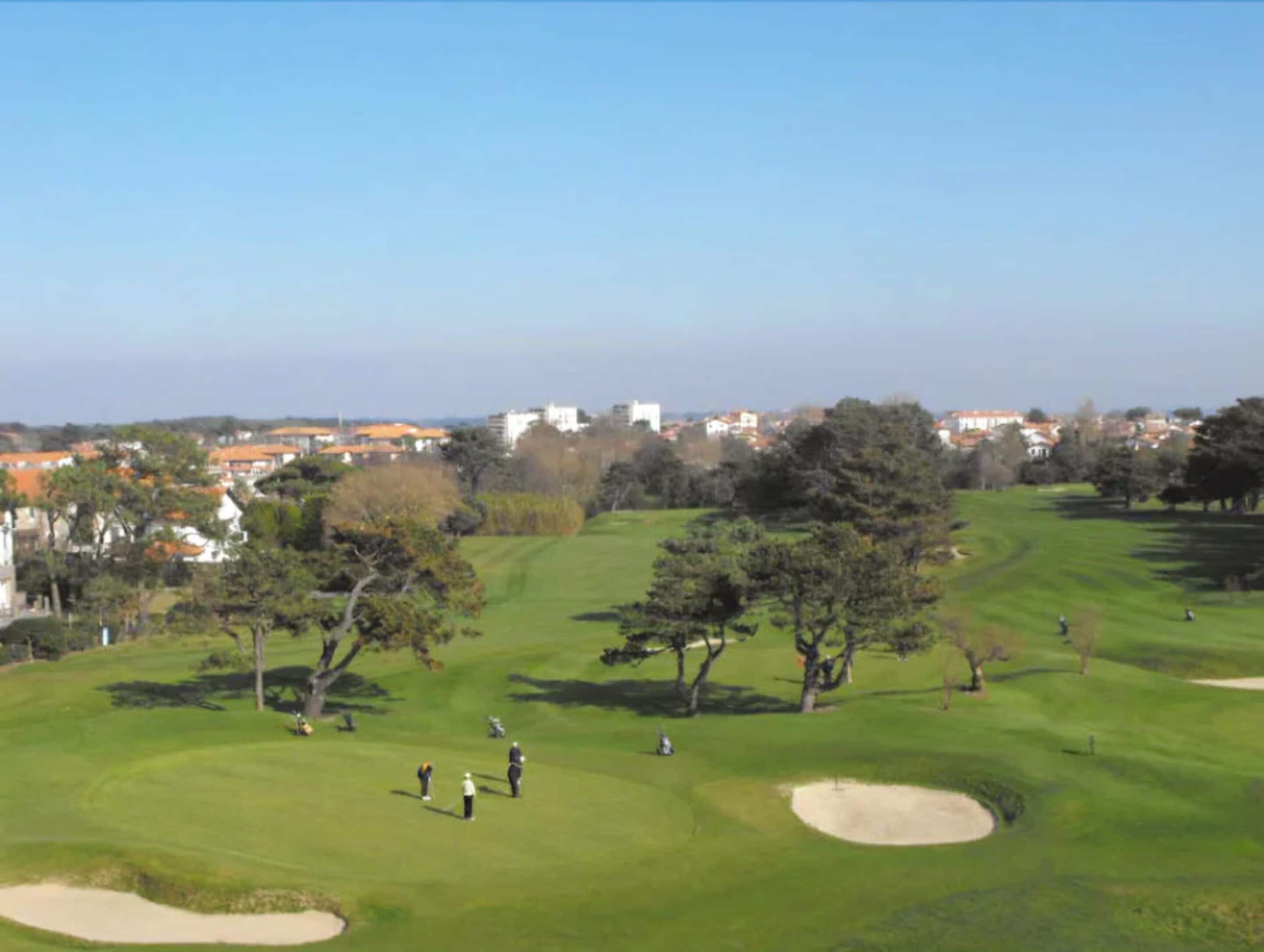 Un parcours de golf avec des bunkers de sable, des arbres et des bâtiments en arrière-plan.