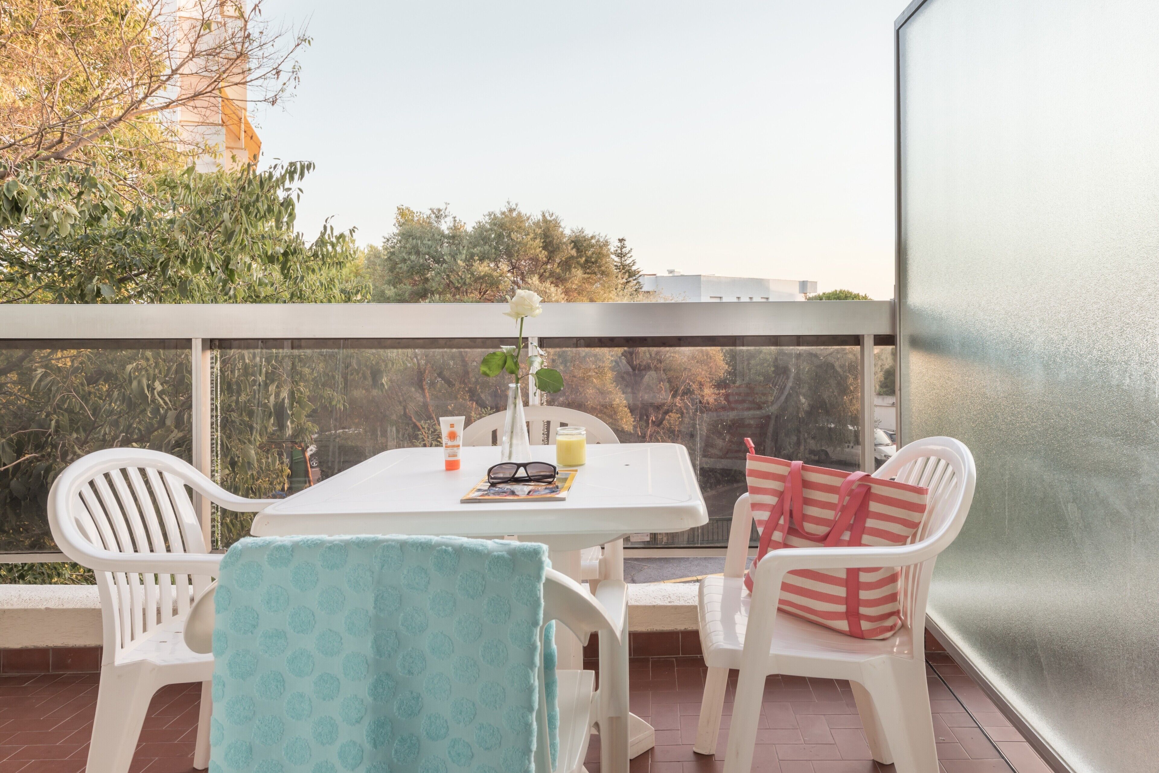Un balcón con mesa, sillas y vistas a árboles y edificios.