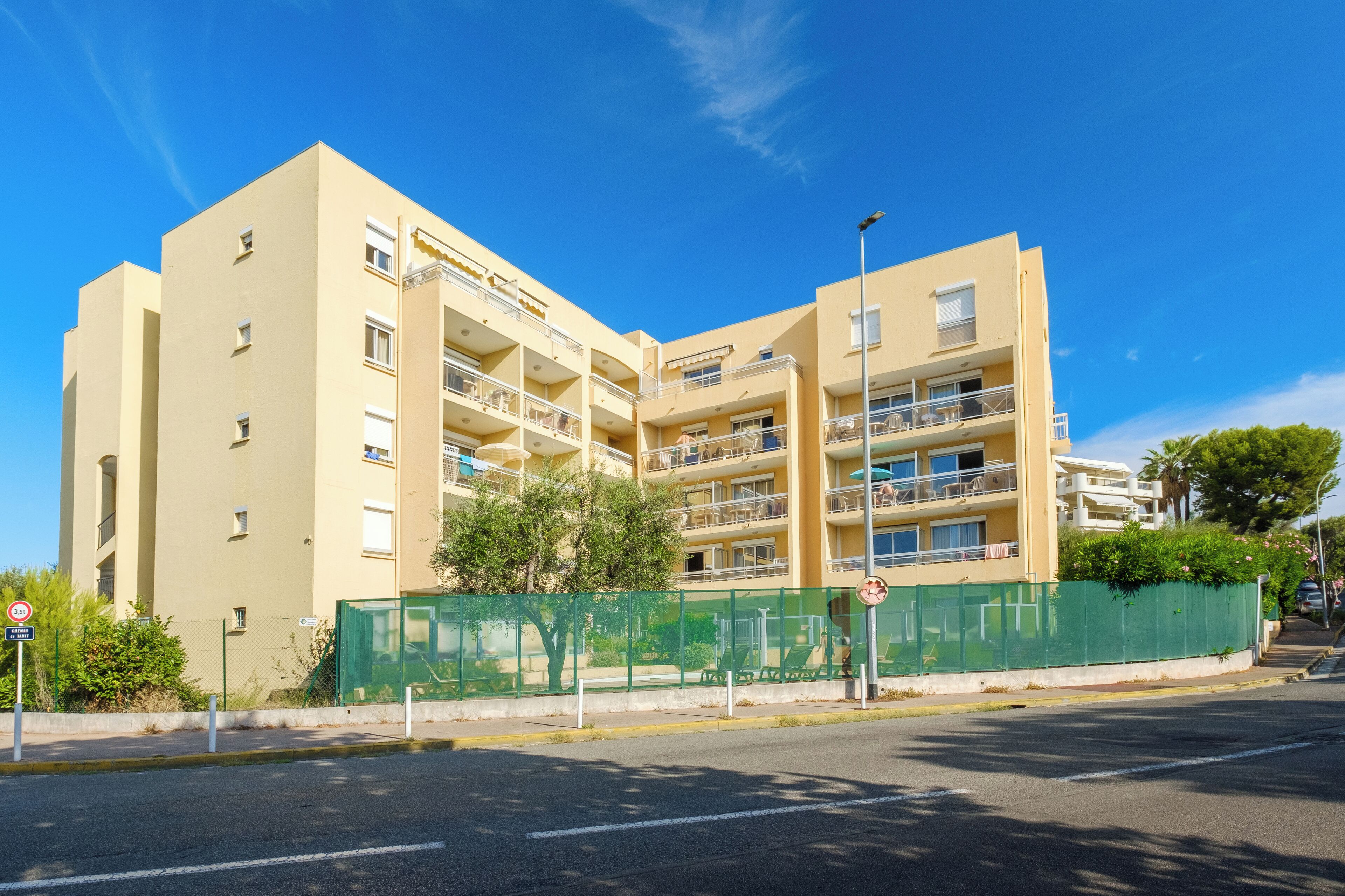 A multi-story hotel with balconies, a green fence, and a clear blue sky.