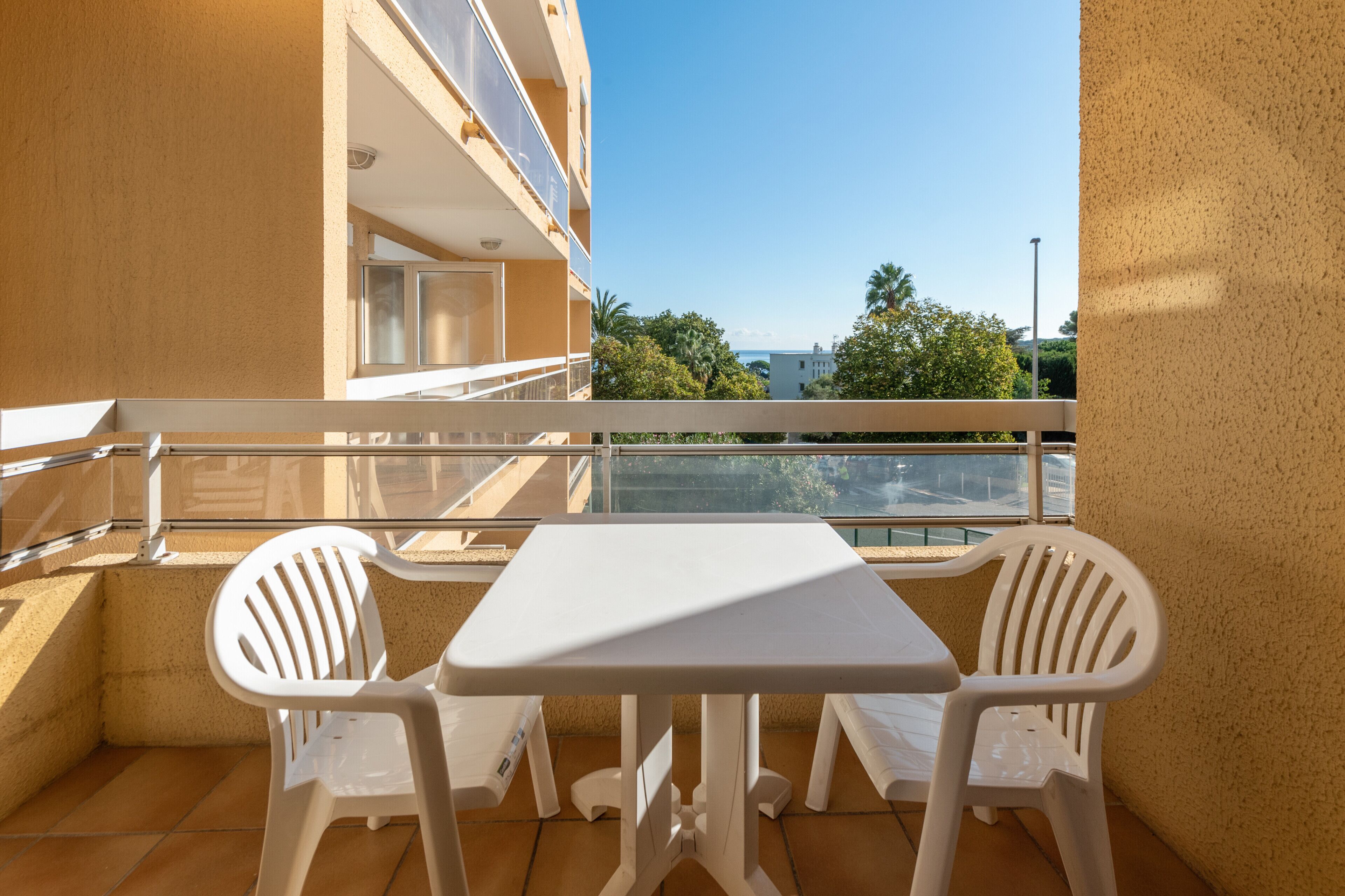 Un balcón con una mesa blanca y dos sillas blancas, con vistas a un edificio y árboles.