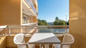 Un balcón con una mesa blanca y dos sillas blancas, con vistas a un edificio y árboles.