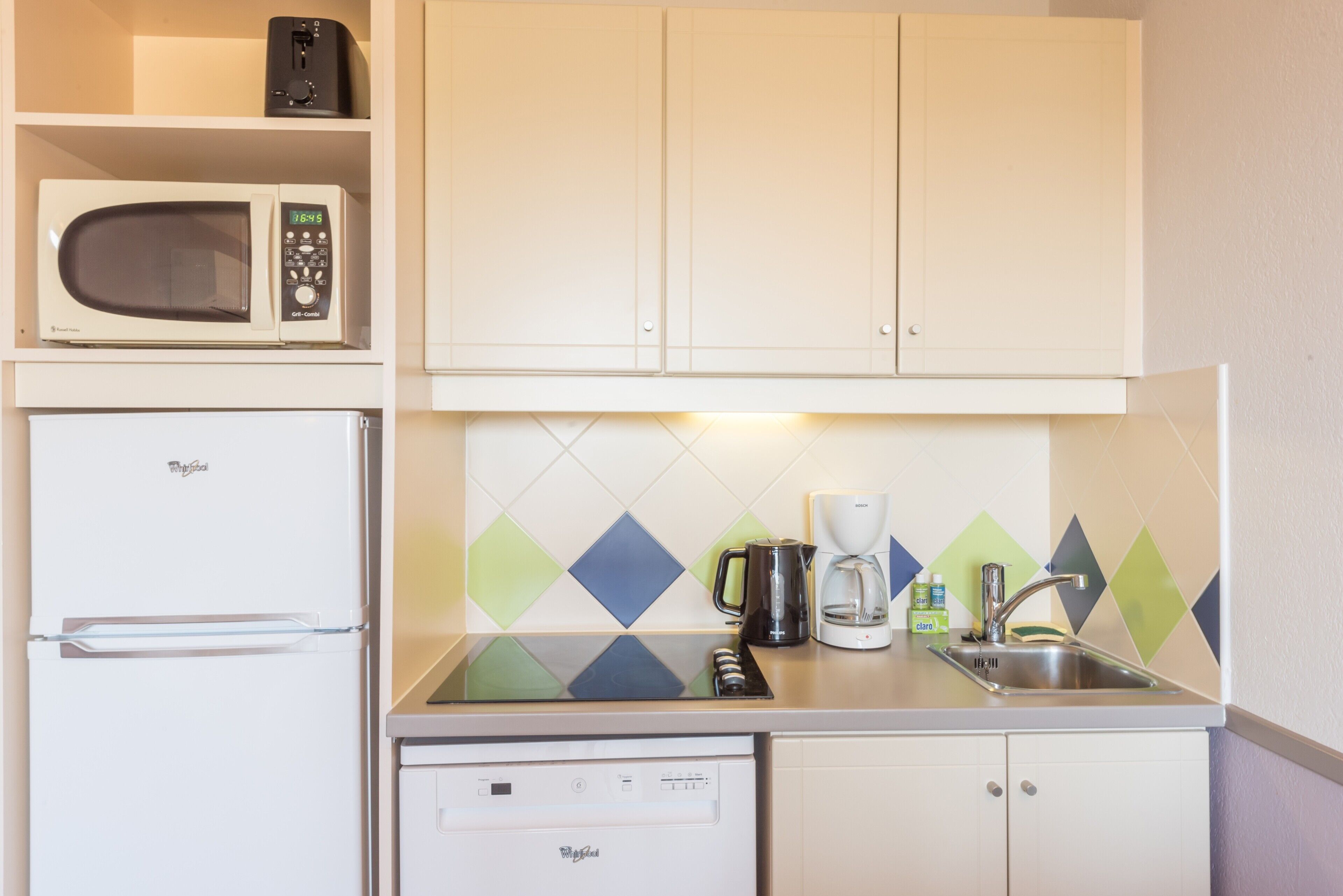 Cocina compacta con microondas, refrigerador, lavavajillas y cafetera sobre la encimera.
