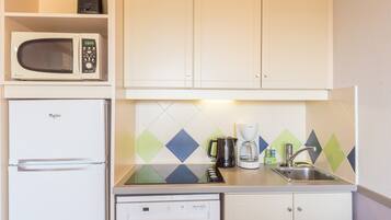 Cocina compacta con microondas, refrigerador, lavavajillas y cafetera sobre la encimera.