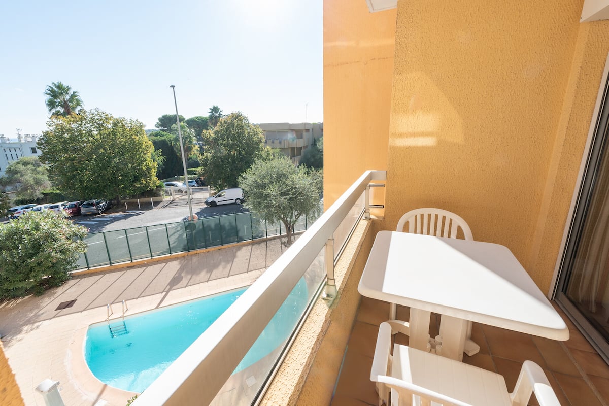 Ein Balkon mit Blick auf einen Pool, weiße Möbel und ein klarer Himmel.