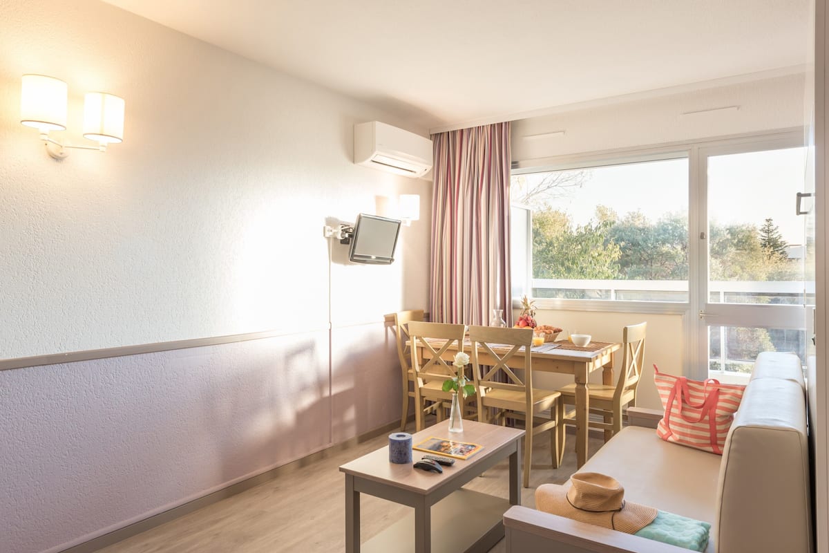 Ein modernes Hotelzimmer mit Essbereich, einer Couch, einem Fernseher und einem Fenster mit Vorhängen.