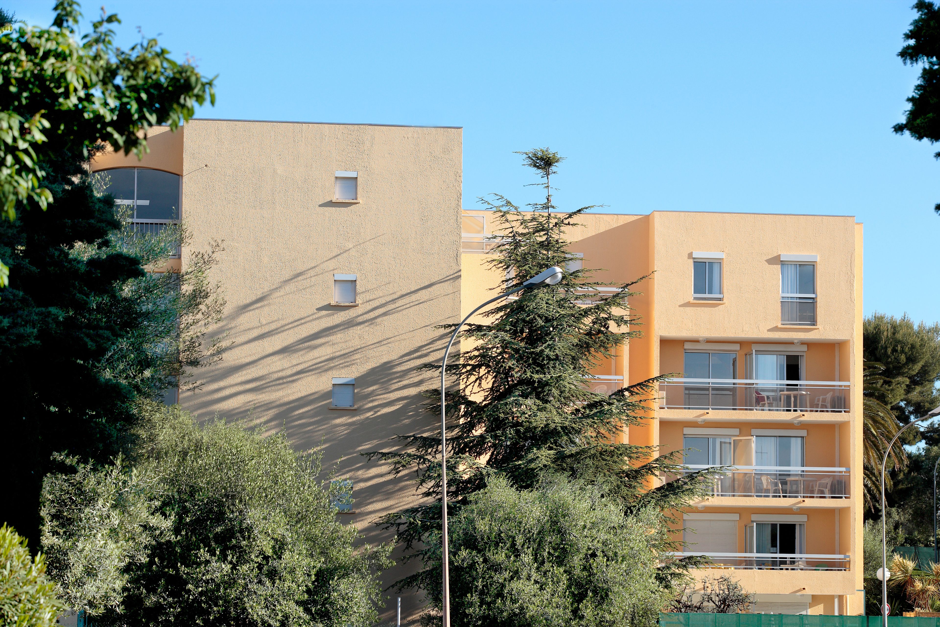 A multi-story building with balconies and large windows, surrounded by trees.