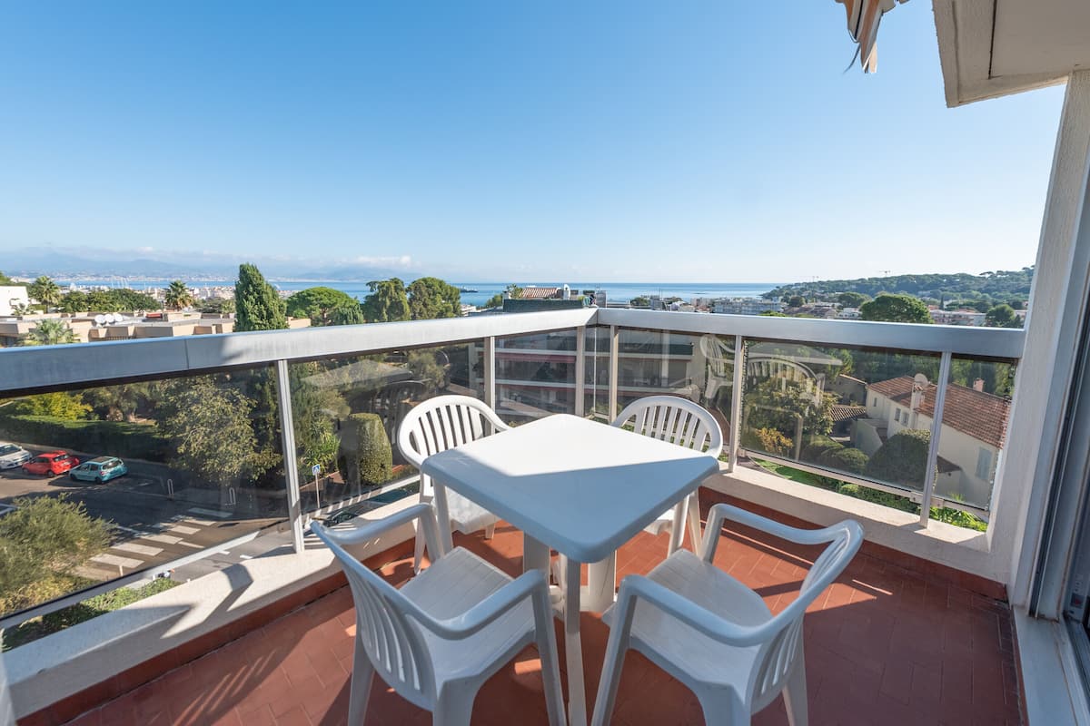 Ein Balkon mit Tisch und Stühlen, der Blick auf das Meer und die umliegenden Gebäude bietet.