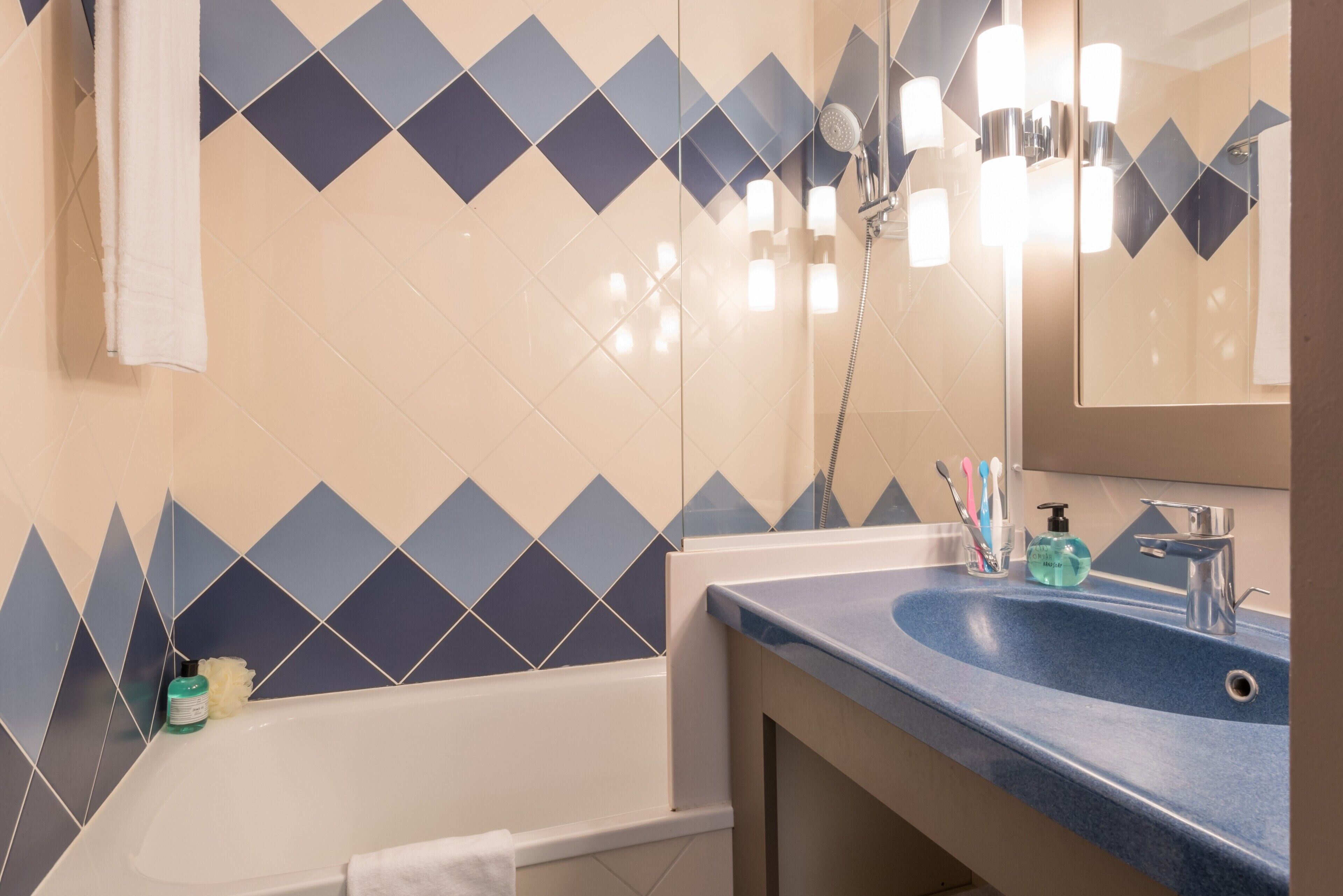 A bathroom with a bathtub, a sink with a blue countertop, and a mirror.