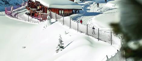 Een besneeuwde lodge met een piste, houten gevel en een omheind gebied.