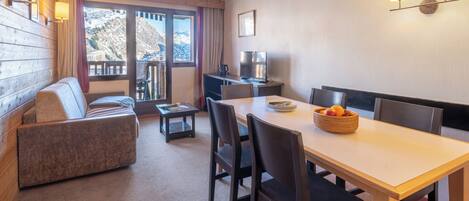 A cozy room with a sofa, a dining table with chairs, a TV, and a window with a mountain view.