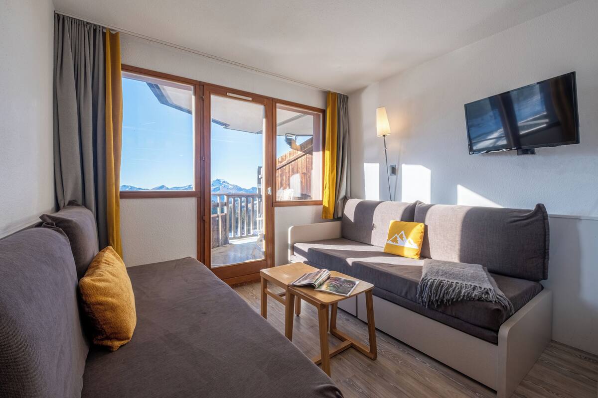 Ein modernes Wohnzimmer mit einer Couch, einem kleinen Sofa, einem Couchtisch aus Holz und einem an der Wand montierten Fernseher.