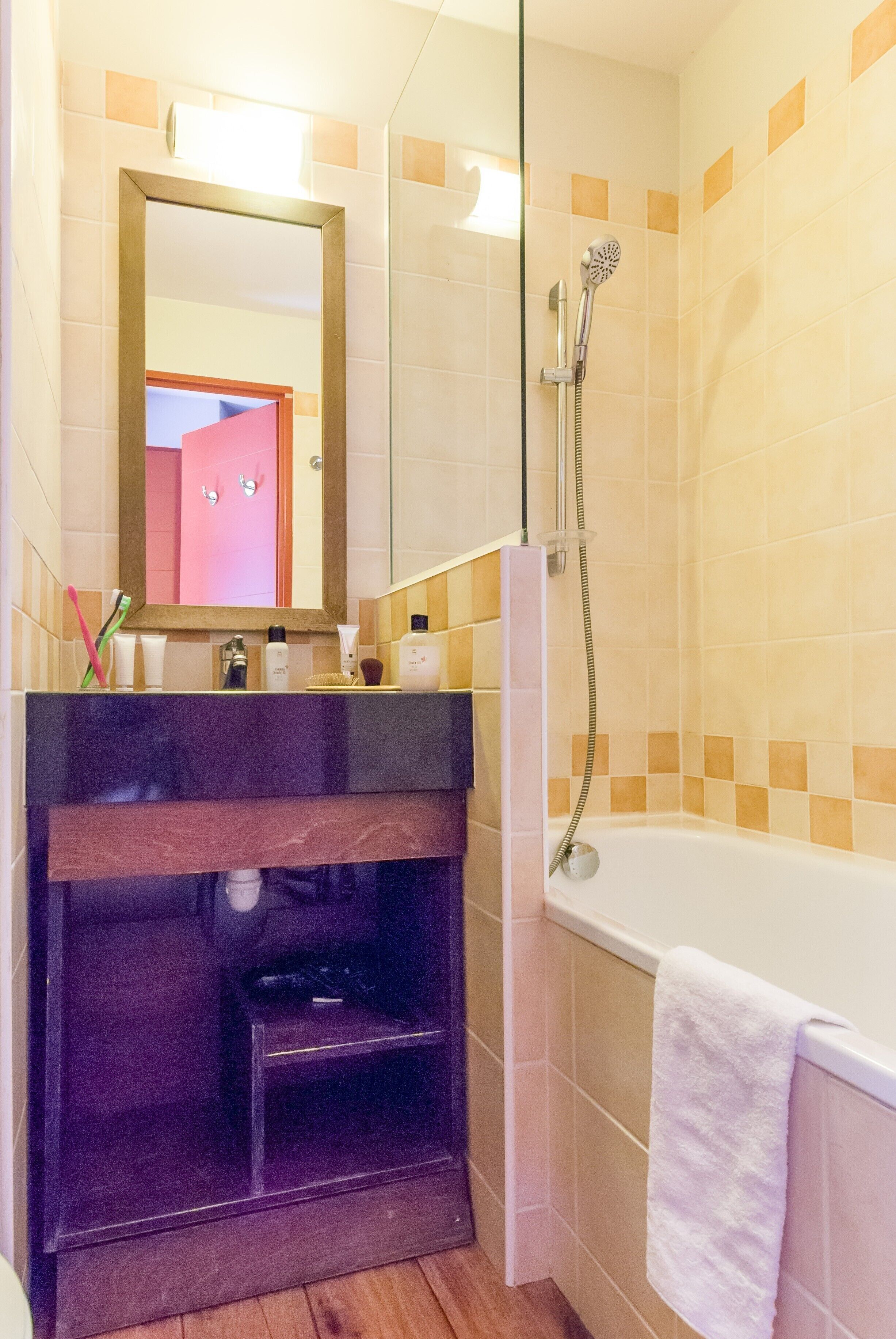 A bathroom with a shower, a sink with toiletries, a mirror, and a towel rack.