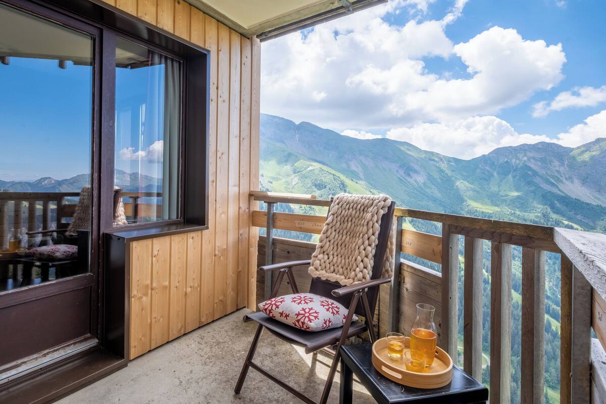 Ein Holzbalkon mit Stuhl und Tisch, einem Bierglas und Blick auf die Berge.