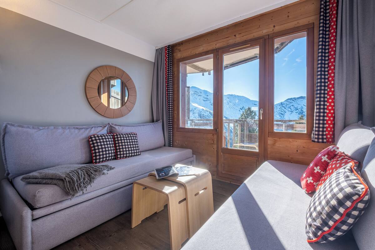 Ein gemütliches Zimmer mit einer Couch, einem kleinen Holztisch und Bergblick durch große Glasfenster.
