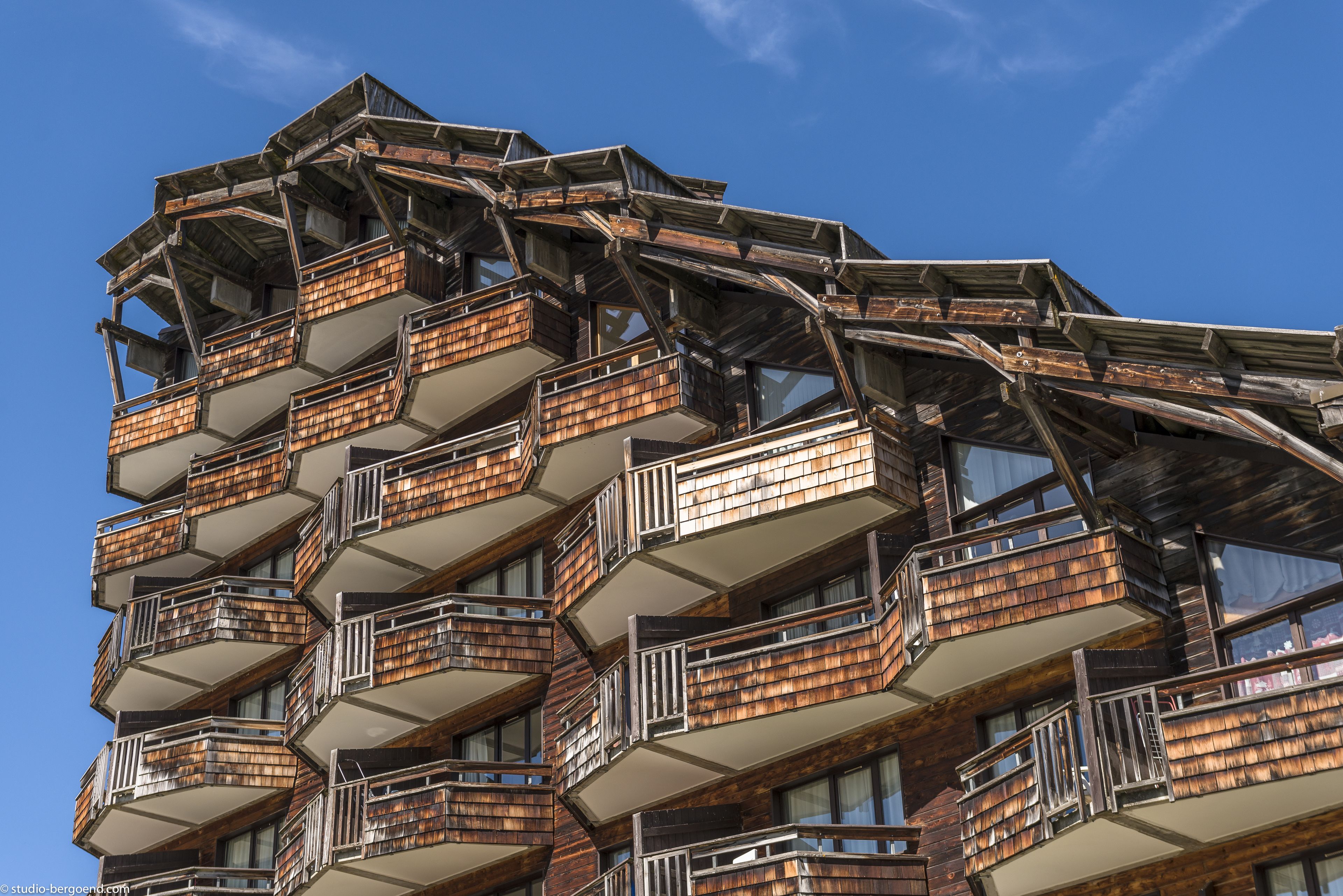 A multi-story building with a unique architectural design featuring wooden balconies and a clear blue sky in the background.