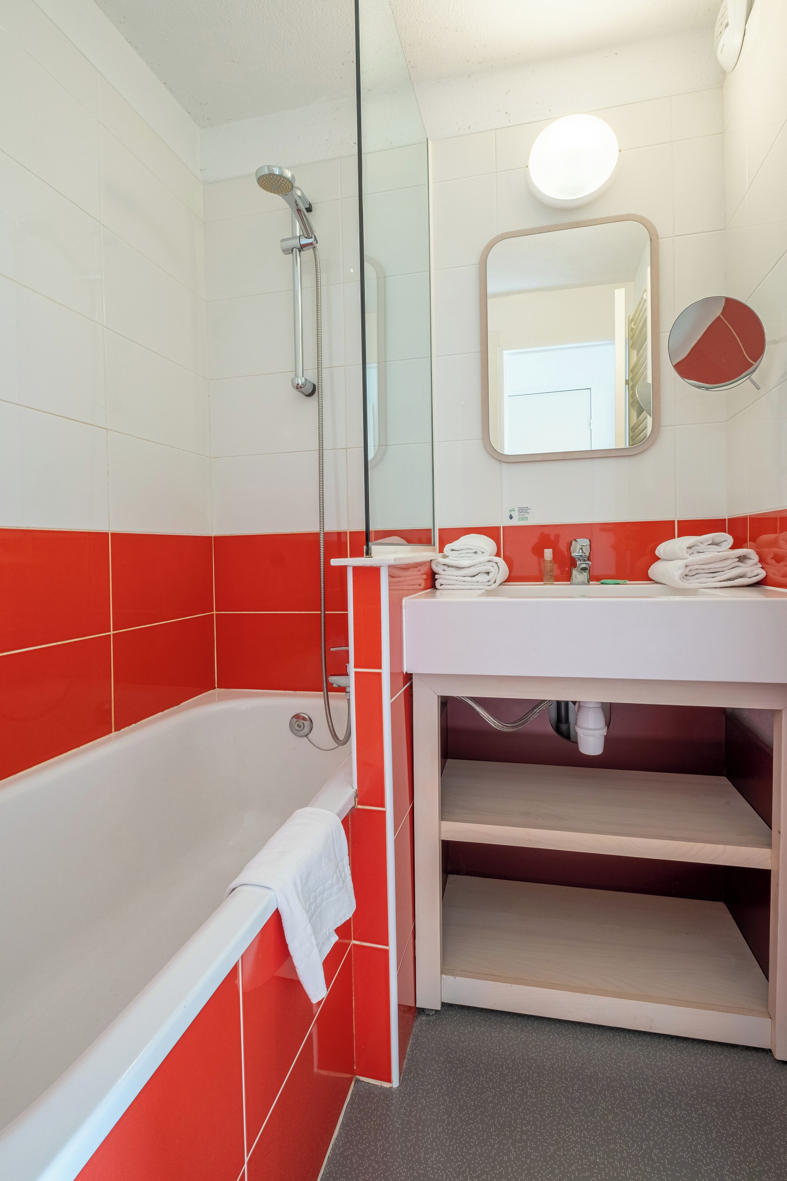 A bathroom with a white bathtub, red tiles, a sink with a mirror, and a towel rack.