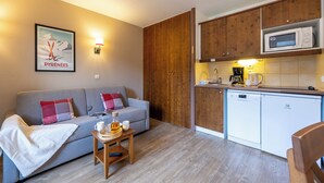Un espacio habitable compacto con sofá, una pequeña mesa de madera con bandeja, microondas y lavavajillas.
