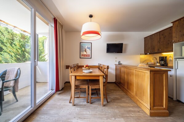 A modern kitchen with wooden cabinets, a dining table, and a large window offering a view of trees.