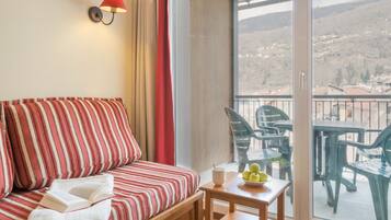 A room with a striped sofa, a small table with a bowl of fruit, and a view of the outside balcony area.