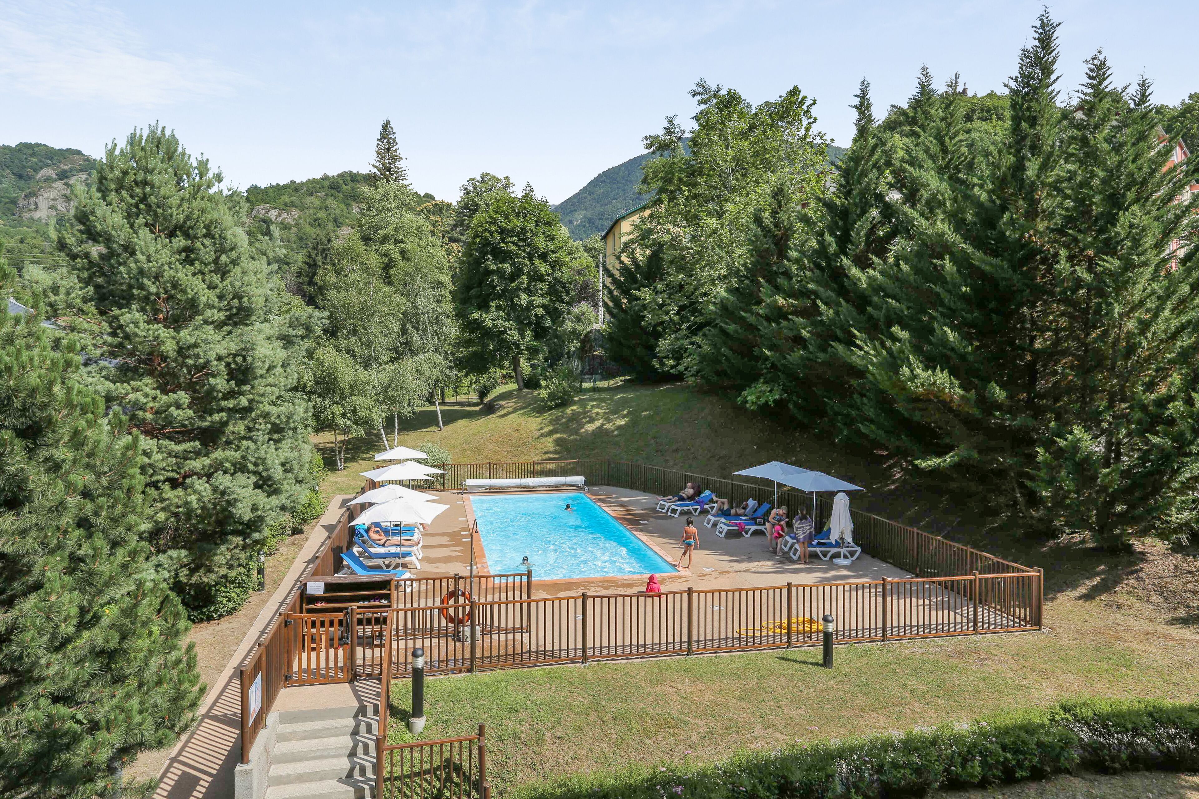 A swimming pool with a deck area, surrounded by trees and a mountainous backdrop.