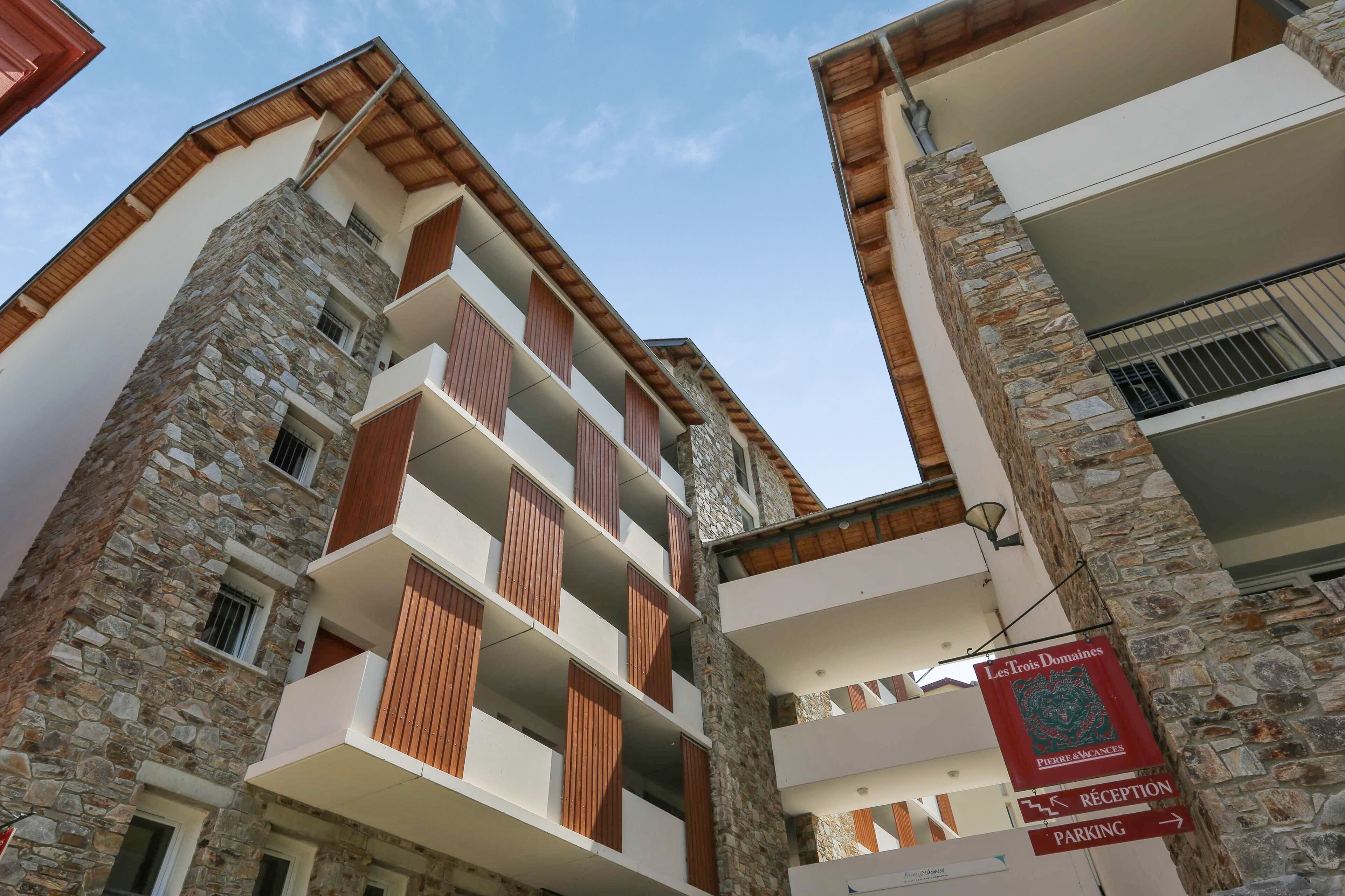 A multi-story building with stone facades, wooden balconies, and a sign indicating a reception and parking area.
