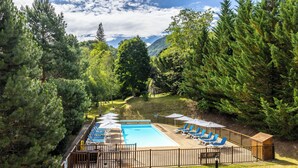 Una piscina con sillas de descanso y sombrillas, rodeada de árboles y una terraza de madera.