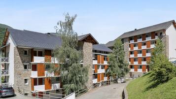 A modern multi-story building with balconies, stone and wood accents, and a parking area.