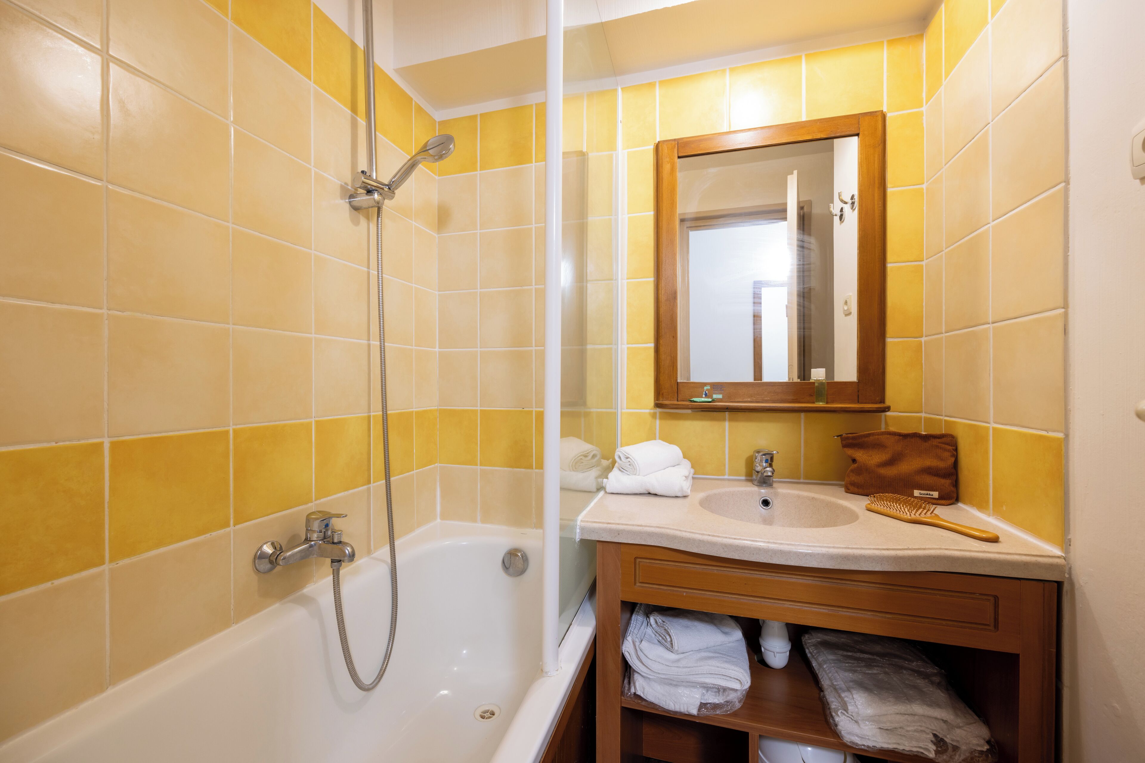 Een badkamer met gele tegels, een badkuip, een wastafel, een spiegel en een handdoekrek.