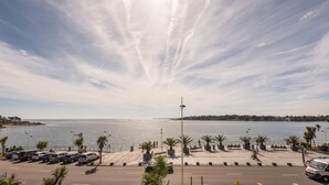 Een waterkantpromenade met geparkeerde auto's, palmbomen en een helder uitzicht op de zee.