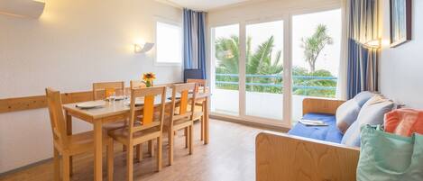 A room with a wooden dining table and chairs, a sofa with a blue cushion, and a window with curtains.