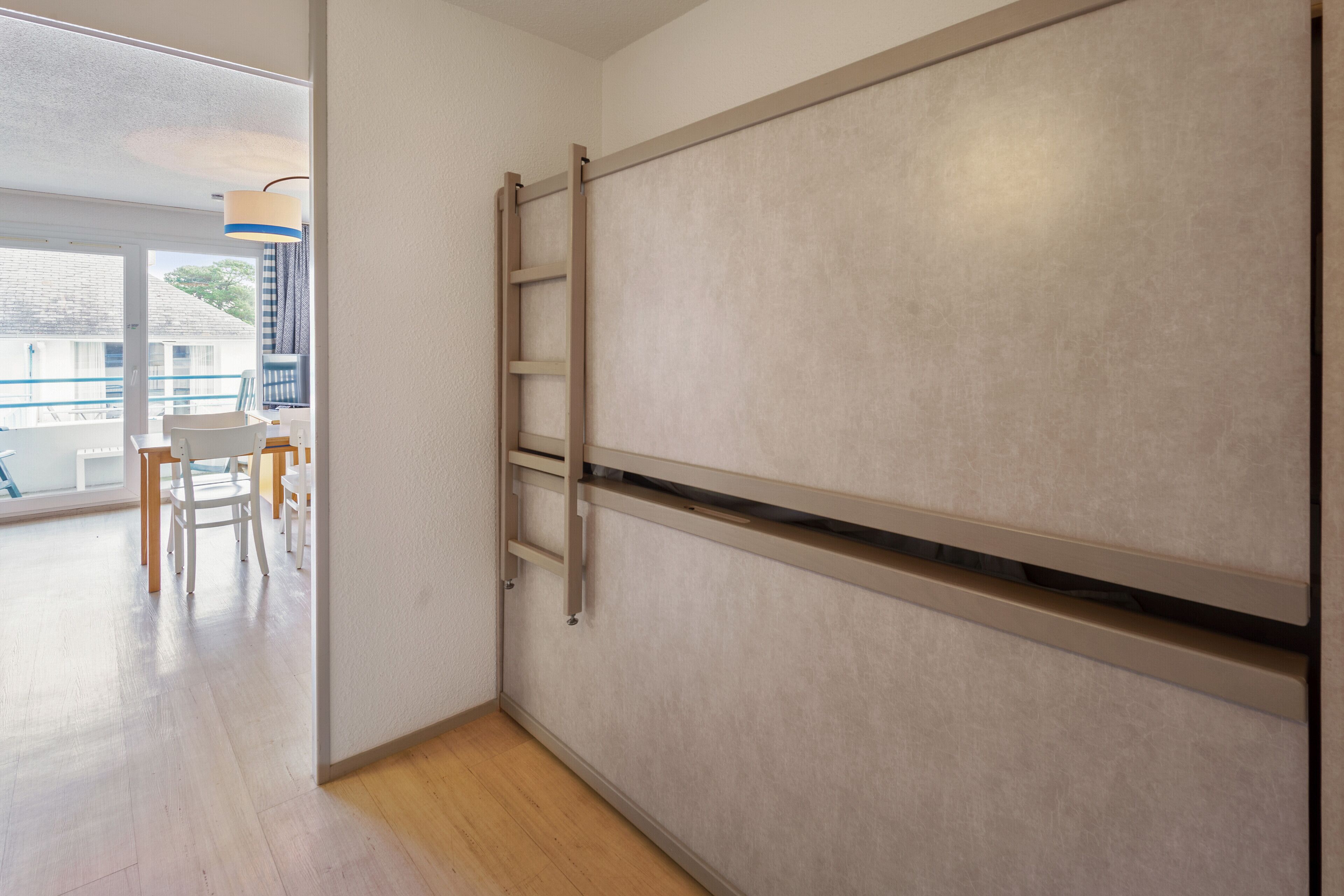 Een kamer met een schuifdeur, een houten vloer en uitzicht op een balkon met stoelen en een tafel.