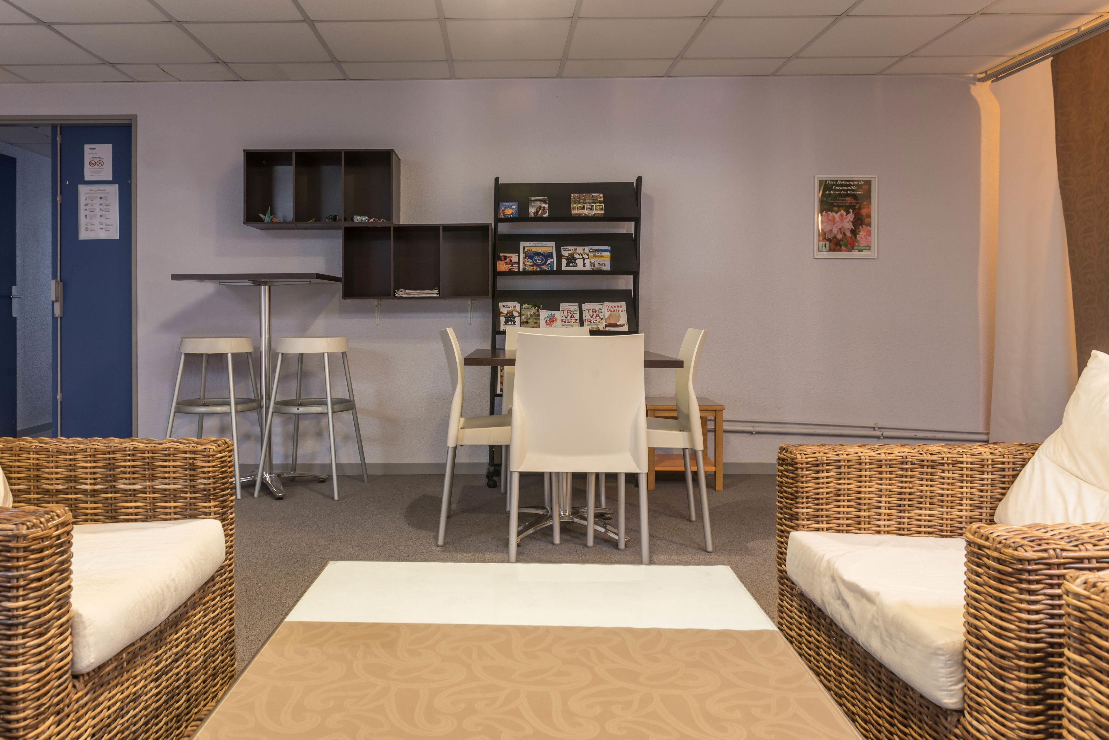Ein Zimmer mit einem Esstisch, vier Stühlen, zwei Korbsesseln, einem Bücherregal und einem kleinen Fernseher auf einem Regal.