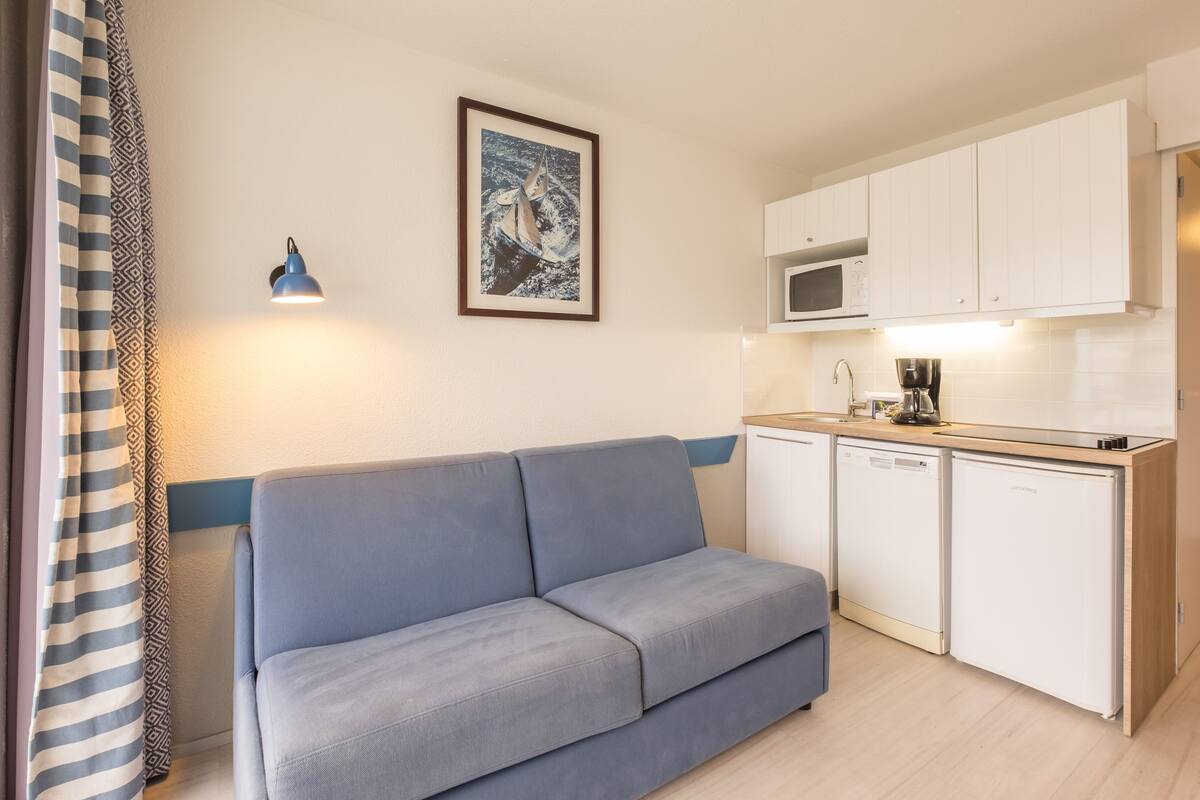 Ein kompakter Wohnbereich mit einer Couch, einer Küchenzeile und einem gerahmten Bild an der Wand.