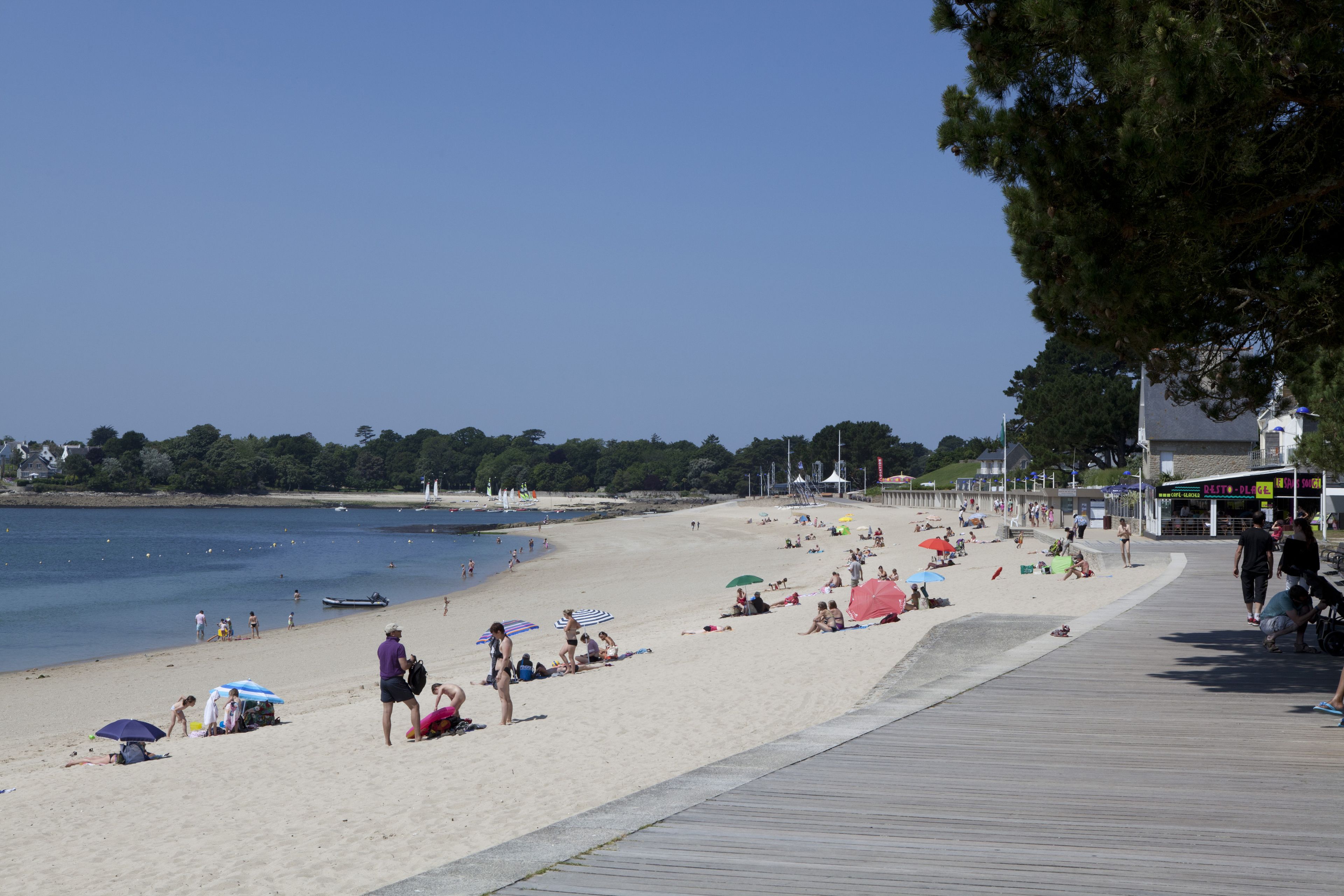 A beach with a wooden boardwalk, people sunbathing, and umbrellas.