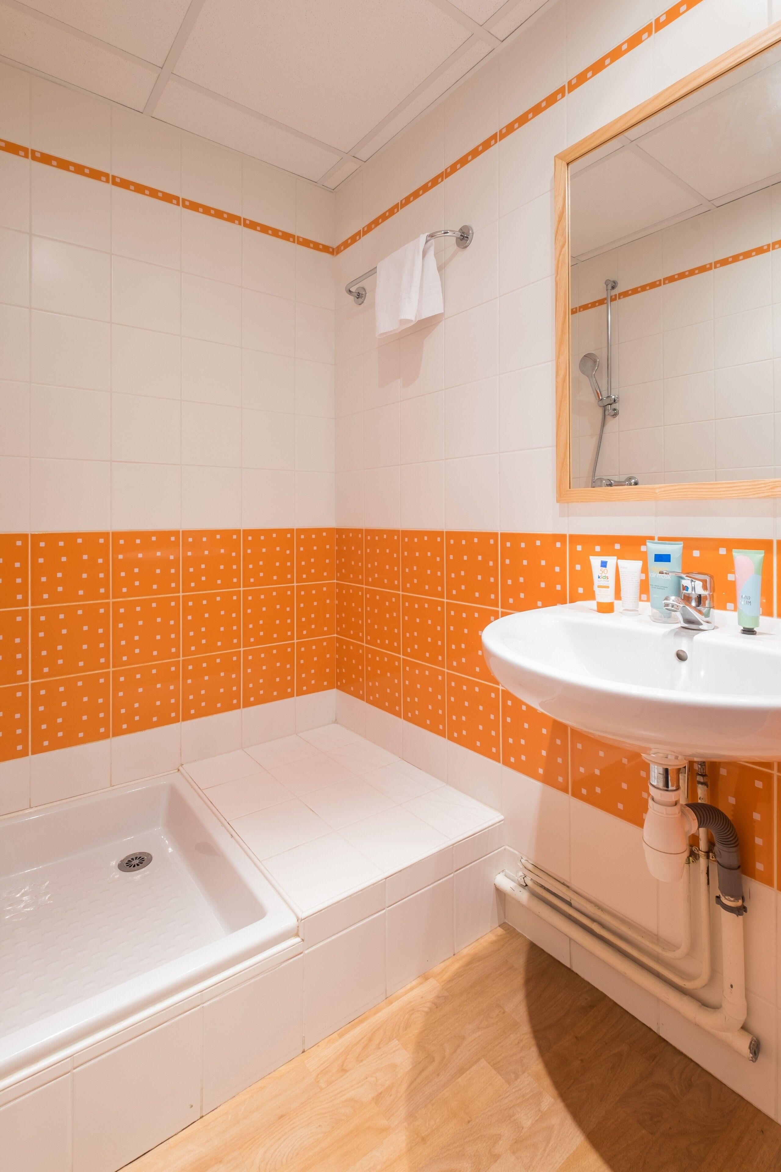 A bathroom with a white sink, a bathtub, and orange patterned tiles.