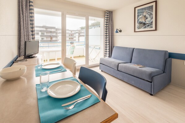 Una sala de estar moderna con comedor, un sofá y un balcón con vistas a edificios.